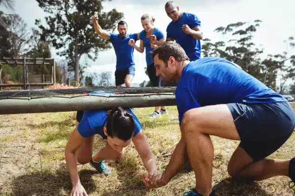 Image of a Group of People Wearing Blue Attending an Outdoor Bootcamp as a Woman is Helped by a Man Under an Obstacle