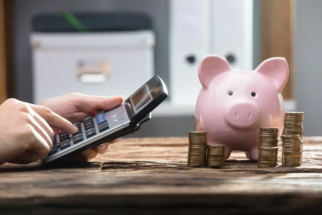 Image of a Piggybank Surrounding by Coins With a Personal Typing on a Calculator Beside It