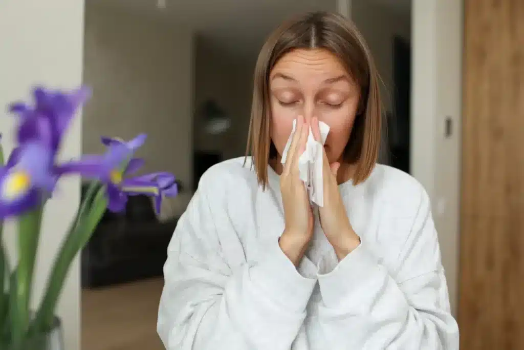Image of a woman with short blonde hair blowing her nose as she suffers from allergies.