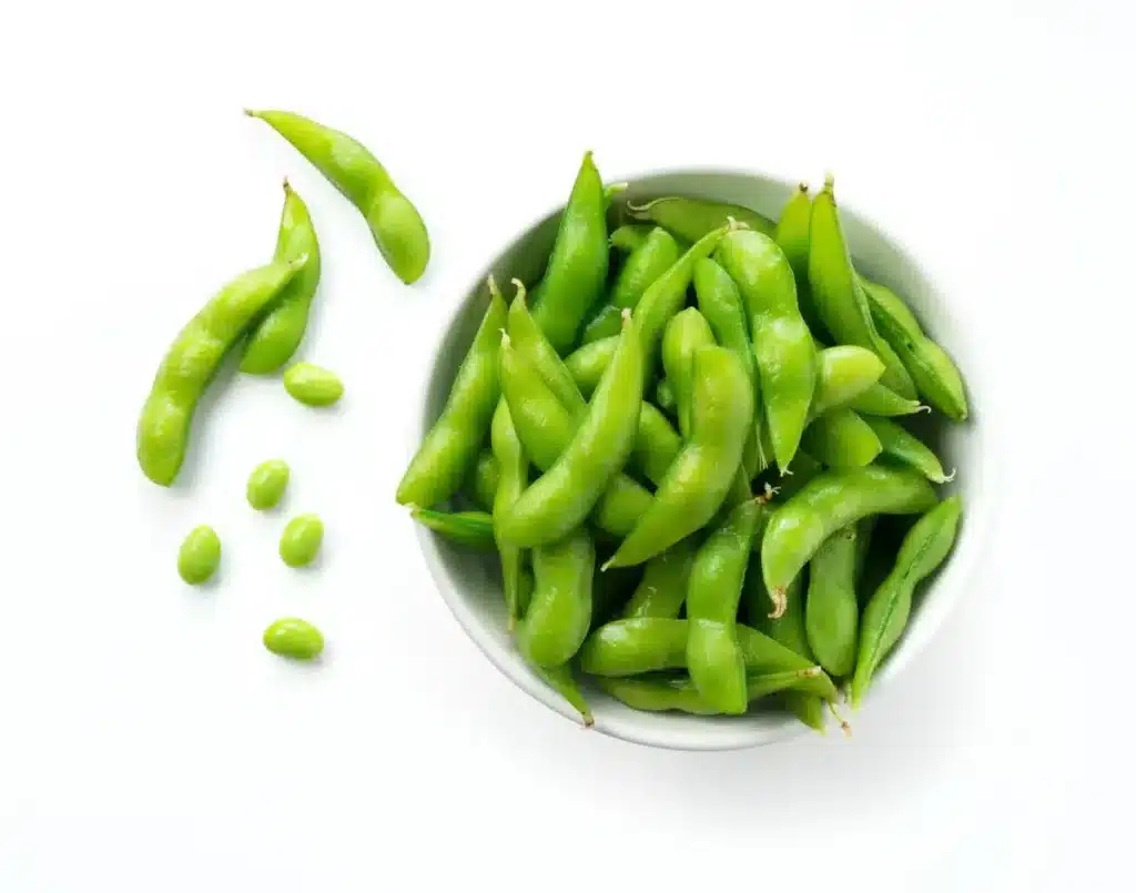 Close Up Image of a Bowl of Green Edamame With a Few Sprinkled Beside It